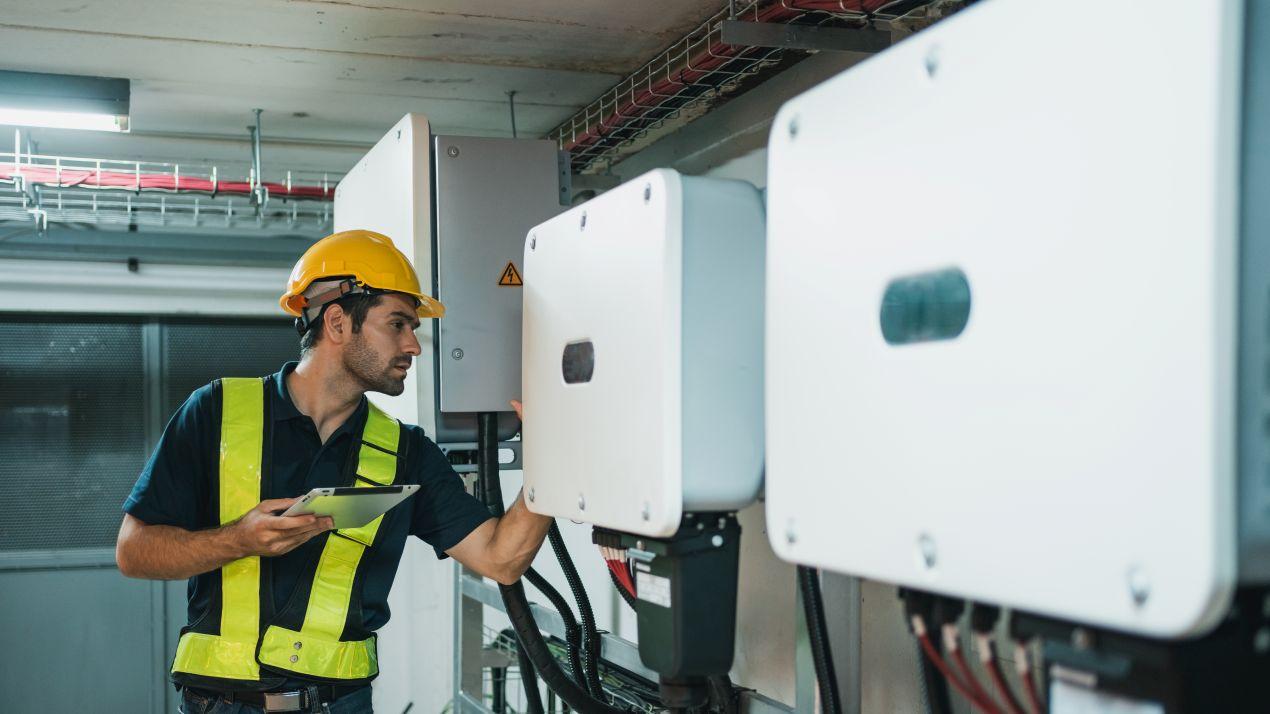 Elektriker kontrolliert Deye Hybrid Wechselrichter in Kellerraum zur Netzrückspeisung und Speichersteuerung