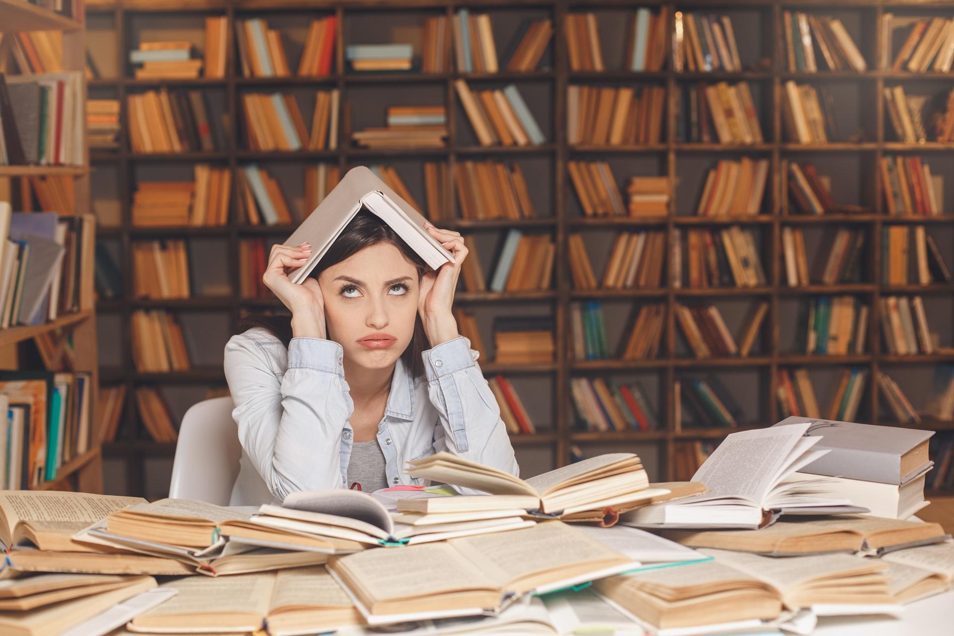 Gestresste Studentin mit Buch in Bibliothek | Ghostwriter Hausarbeit