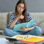 Studentin lernt mit Heften und Laptop auf Sofa | Ghostwriter Hausarbeit