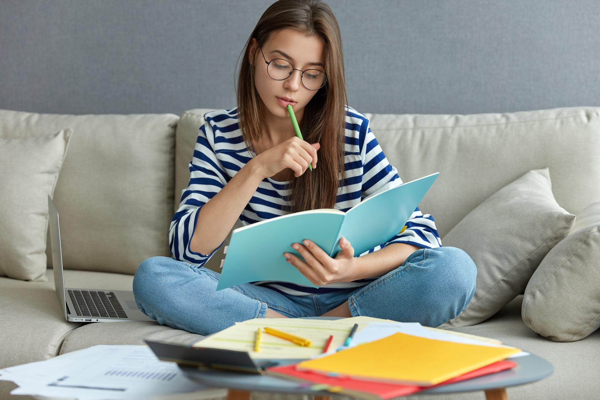 Studentin lernt mit Heften und Laptop auf Sofa | Ghostwriter Hausarbeit