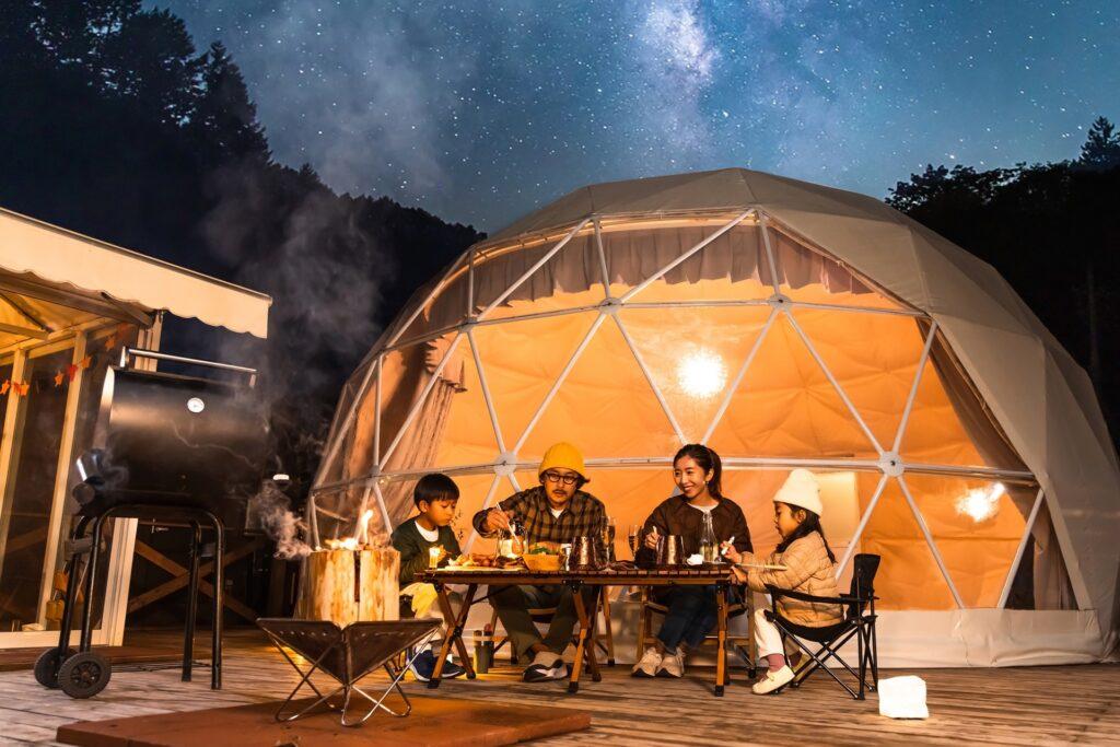 Familie sitzt beim Glamping am Tisch unter Sternenhimmel | Petroleum