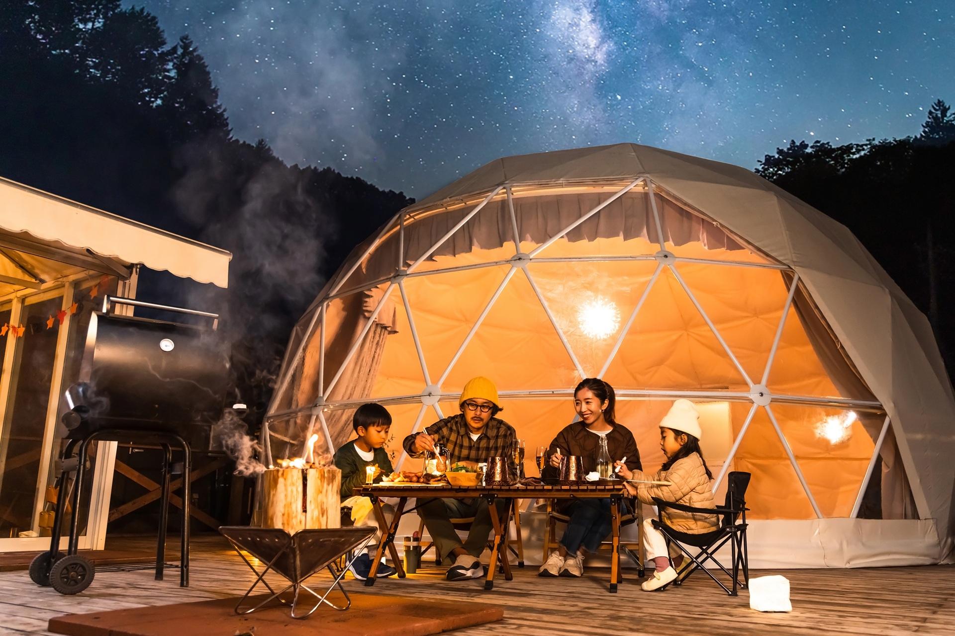 Familie sitzt beim Glamping am Tisch unter Sternenhimmel | Petroleum