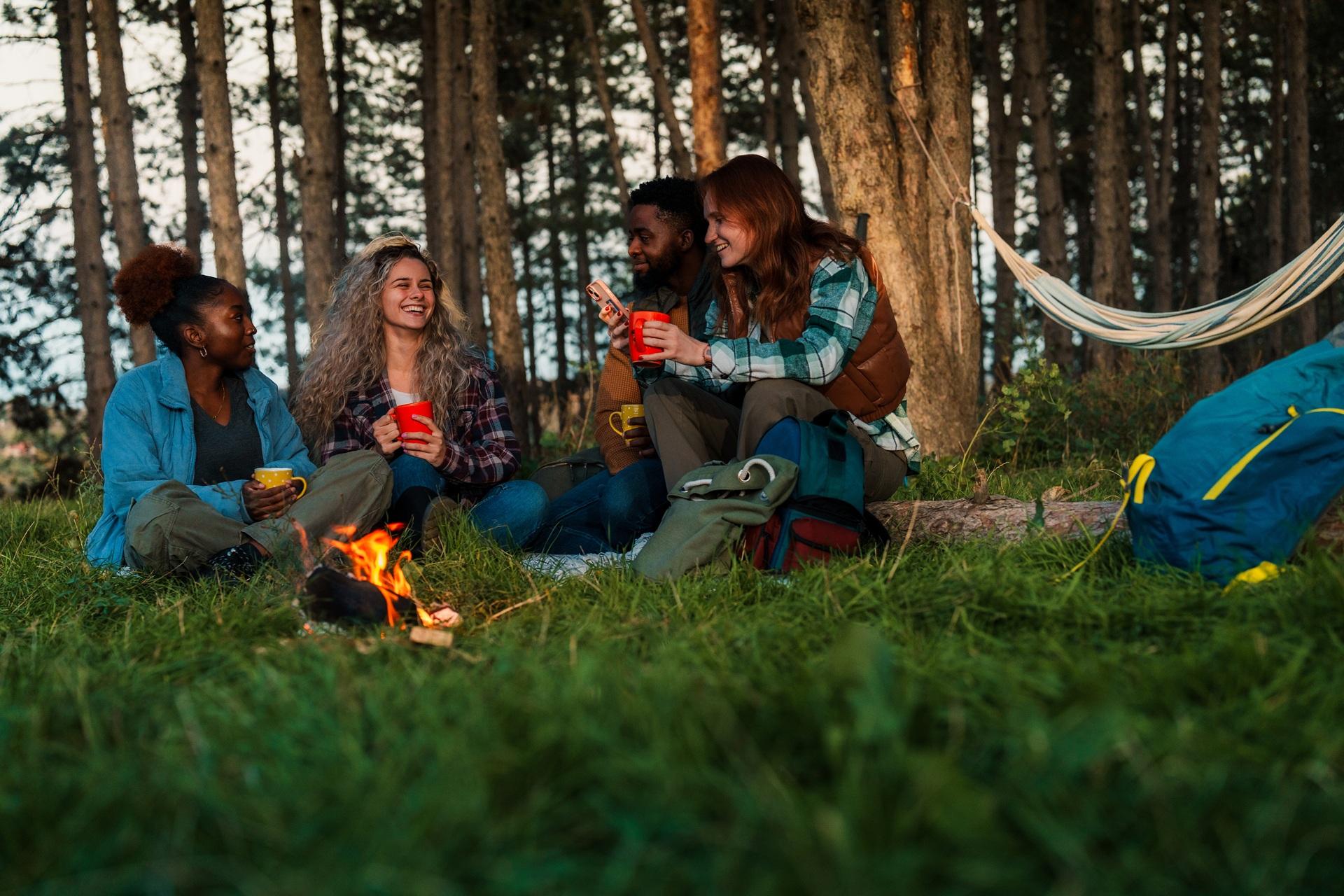 Freunde sitzen am Lagerfeuer und trinken aus Bechern | Petroleum
